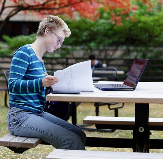 Person seated outdoors at a picnic table, reviewing notes on paper.