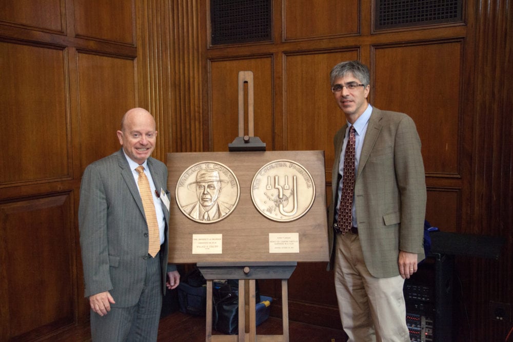 Two faculty standing next to a large award